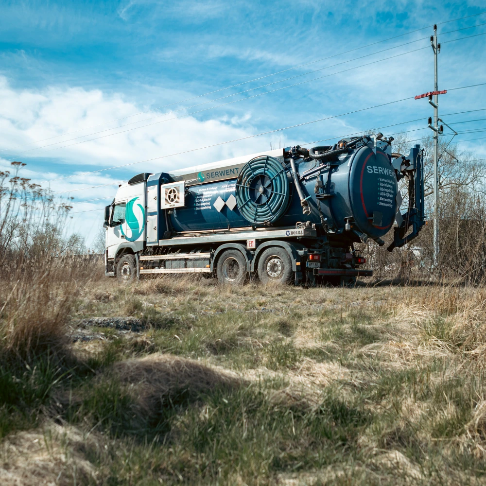 En stor industrisugbil med SERWENT-märke står parkerad på en gräsmatta under en blå himmel, nära elstolpar och elledningar.