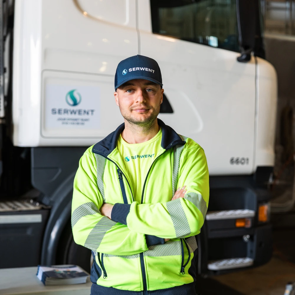 En man i varseljacka och mörkblå keps står med armarna i kors framför en vit lastbil från Serwent i Rotebro och ler lite när logotypen visas på dörren.