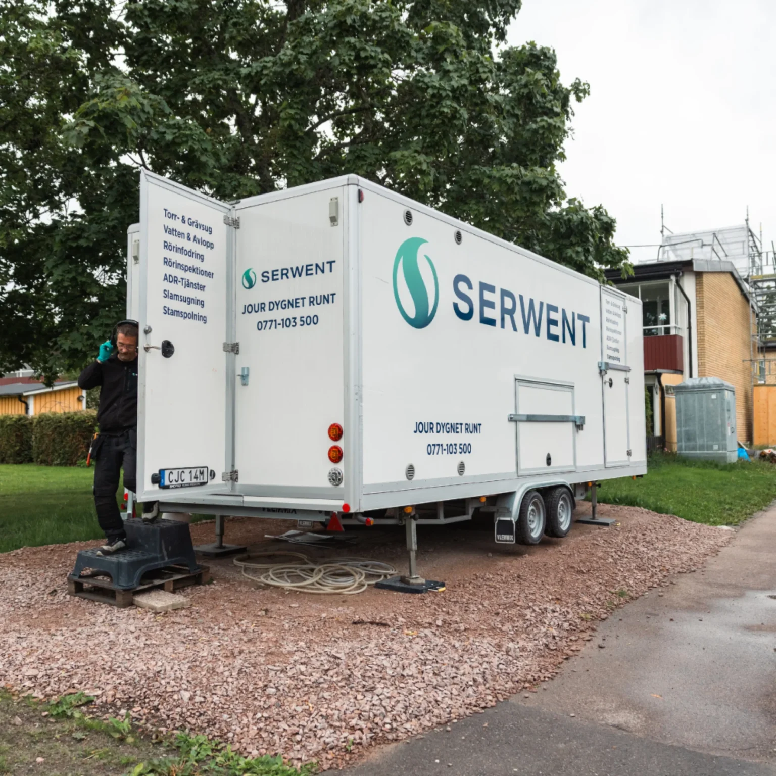 En mobil servicevagn märkt "SERWENT" är parkerad på en grusplan nära träd och byggnader. En man står bredvid trailern, som visar kontaktinformation och svensk text som beskriver tillgängliga tjänster.