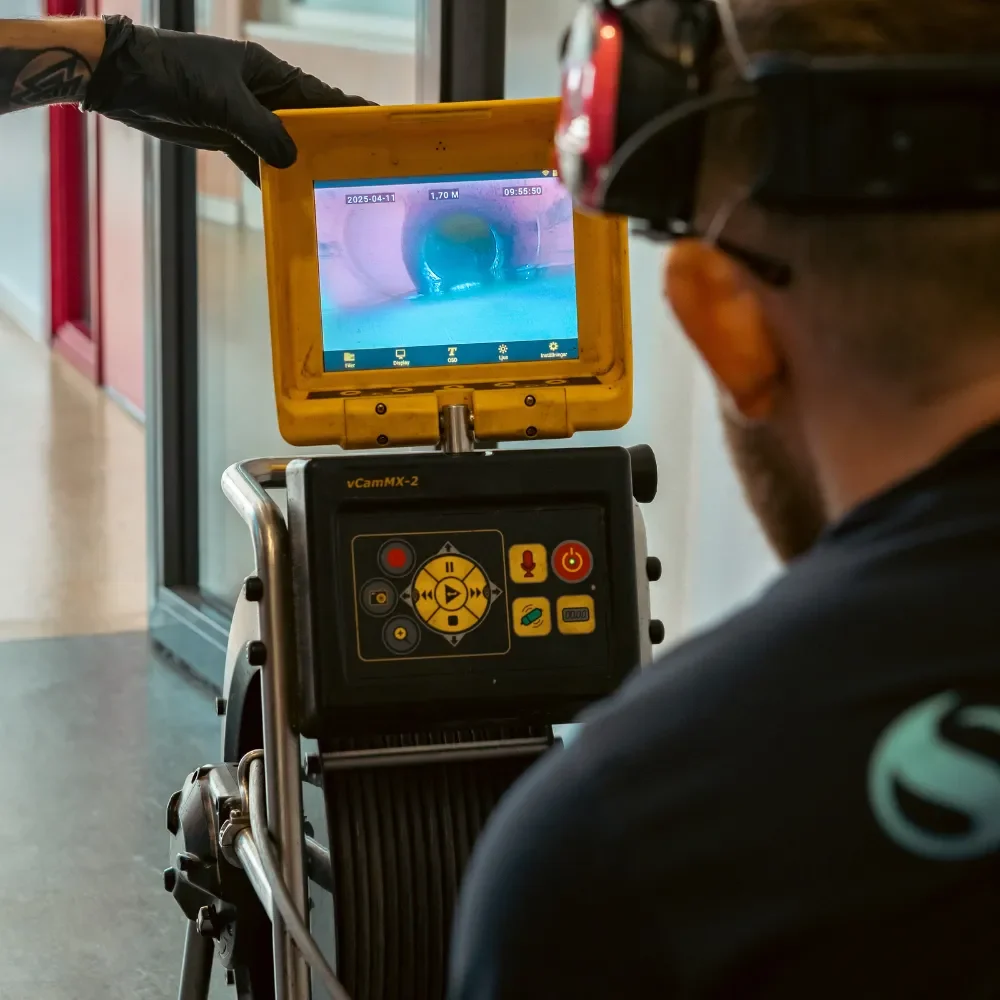 Rörinspektion En person som bär handskar och använder en kamerainspektionsenhet tittar på ett rörs insida på en bildskärm och kontrollerar sannolikt blockeringar eller problem i rörsystemet.